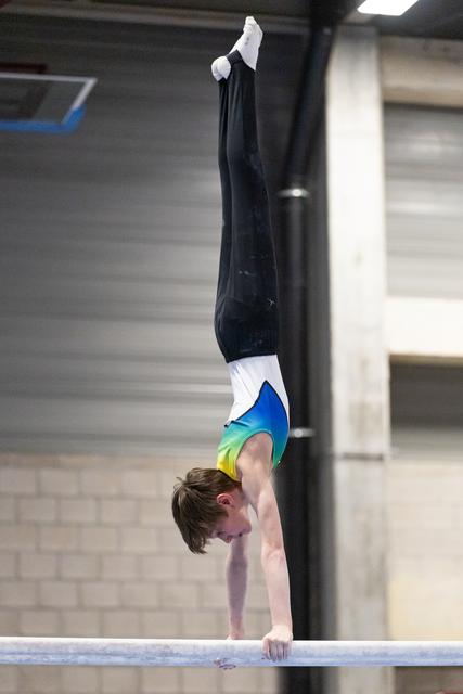Young gymnast performs a perfect handstand on the high bar, body fully extended with legs vertical and toes pointed.