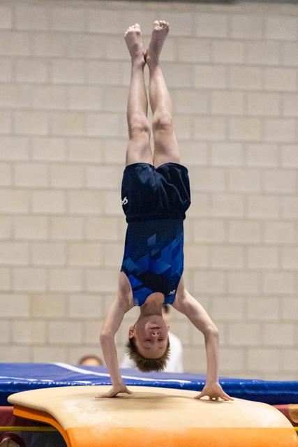 Young gymnast performing a handstand on vaulting equipment, legs extended vertically with pointed toes in indoor gym
