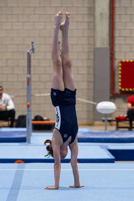 Young gymnast performs handstand on floor exercise mat, demonstrating strength and balance during training session