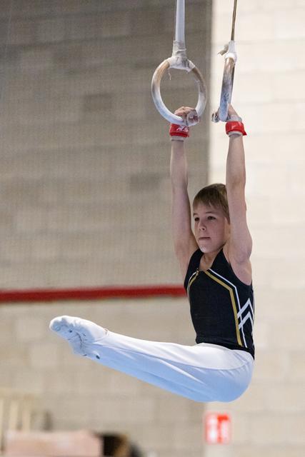 Young gymnast performs on rings with extended legs and pointed toes, showing concentration during routine in training facility