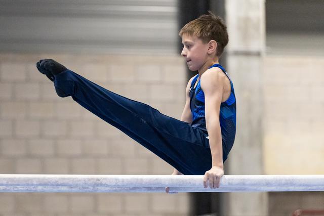 Young male gymnast performing a horizontal bar routine with extended legs, demonstrating strength and control during practice