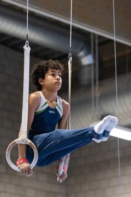 Young gymnast maintains horizontal L-sit position on rings, displaying strength and concentration during training