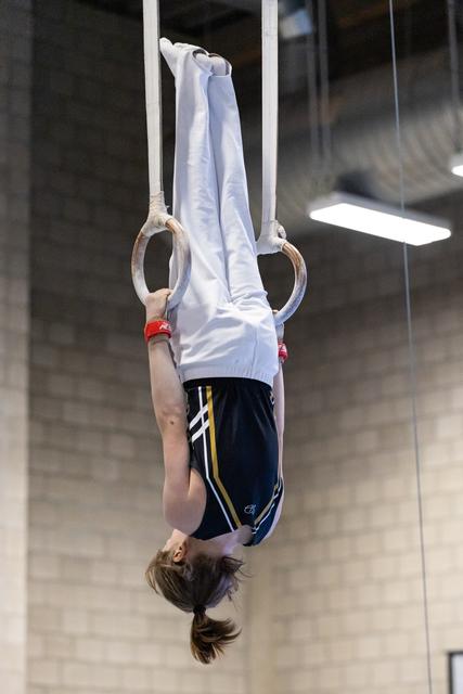 Young gymnast hanging upside down on rings, demonstrating core strength and control during training session