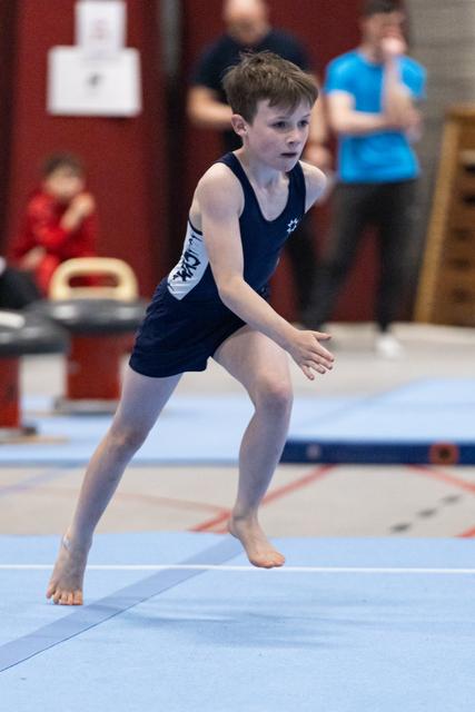 Young gymnast in navy leotard landing with focused expression during floor routine at indoor gymnastics meet