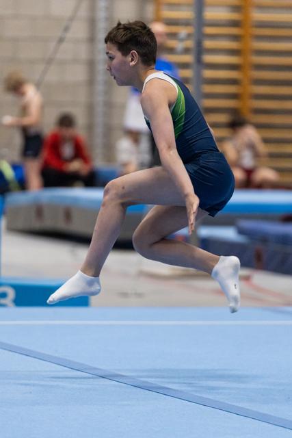 Young gymnast lands a jump during floor exercise routine, showing focused concentration and athletic form in training facility