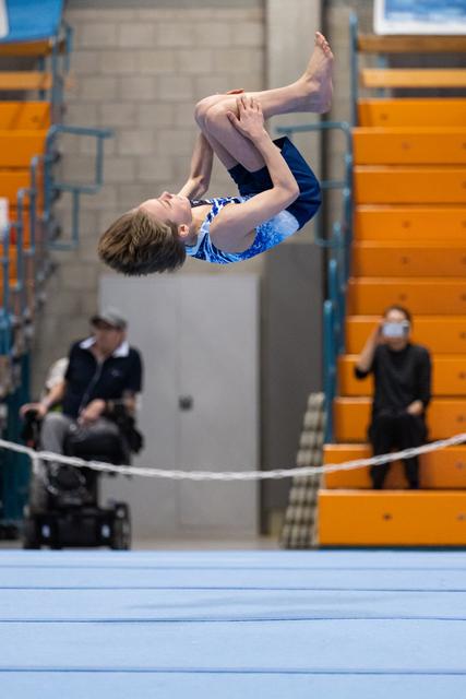 Young gymnast executes a tight tuck position mid-air during floor routine, demonstrating core control in gymnasium