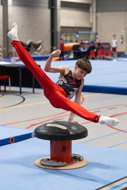 Young gymnast in red pants and sparkly leotard performs a dynamic mushroom circle with legs extended in a training facility