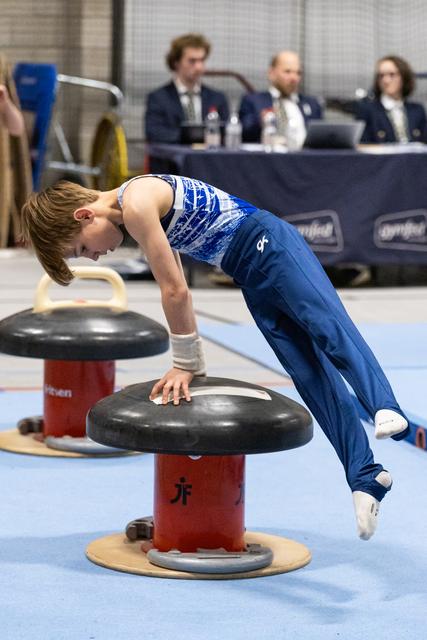 Young gymnast performing circles on mushroom apparatus with intense concentration while judges observe in background