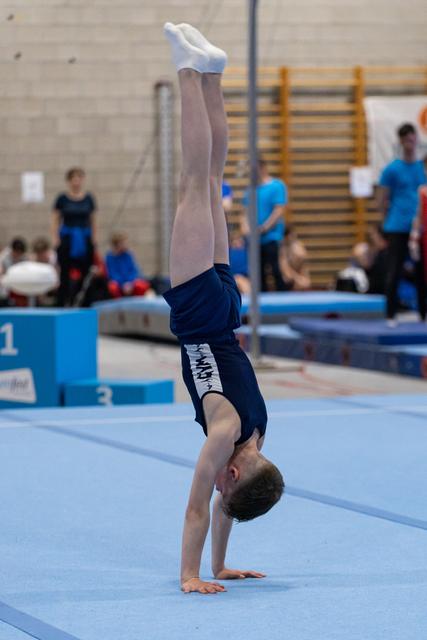 Young gymnast executing a vertical handstand on blue floor mat during practice session in gymnasium