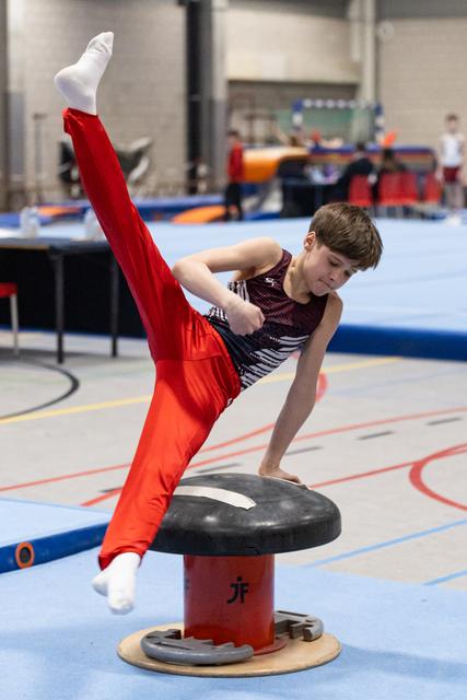 Young gymnast in red pants and sparkly leotard performs a high leg extension on mushroom apparatus during training