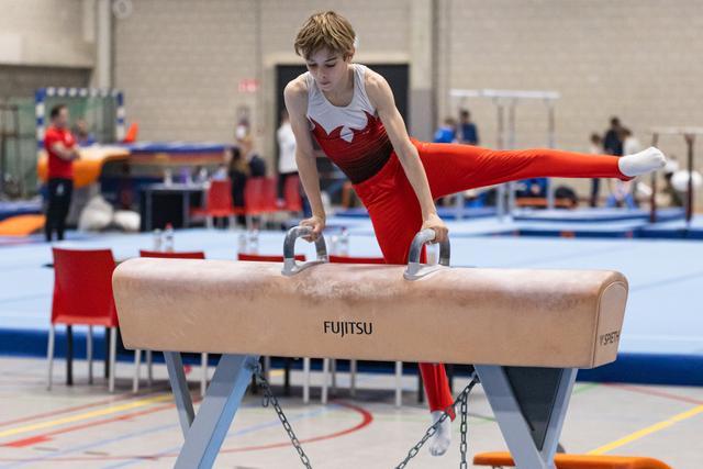 Young male gymnast in red uniform executes a horizontal hold on pommel horse, demonstrating strength and control in training facility