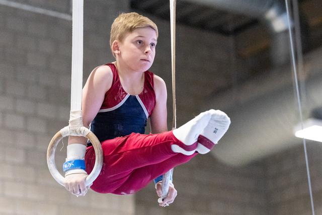 Young gymnast performing on rings with extended legs, demonstrating strength and control during routine