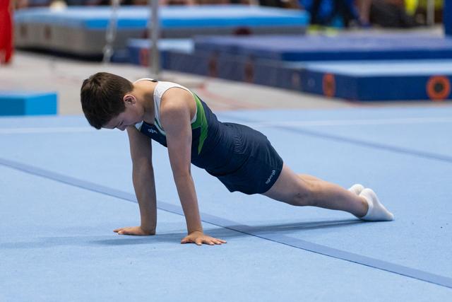 Young male gymnast holds a plank position on blue floor mat, demonstrating strength and concentration during training
