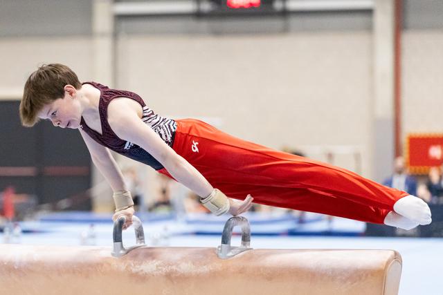 Young gymnast performs L-sit on pommel horse handles, displaying strength and concentration during routine