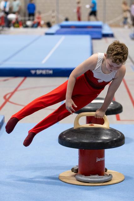 Young gymnast in red and white uniform performs horizontal support position on pommel horse during practice
