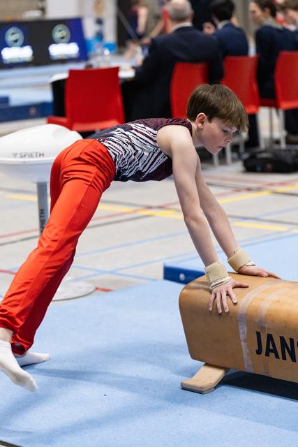 Young gymnast in orange pants holds a plank position on the pommel horse during training, focused and determined