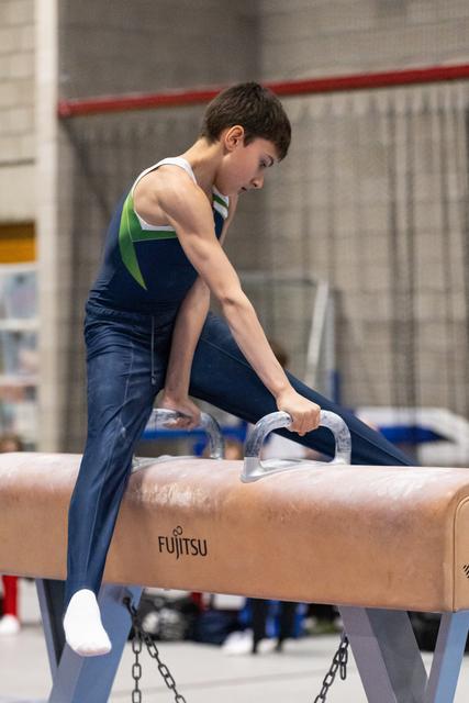 Young male gymnast grips pommel horse handles, focusing intently before his routine in navy and green leotard