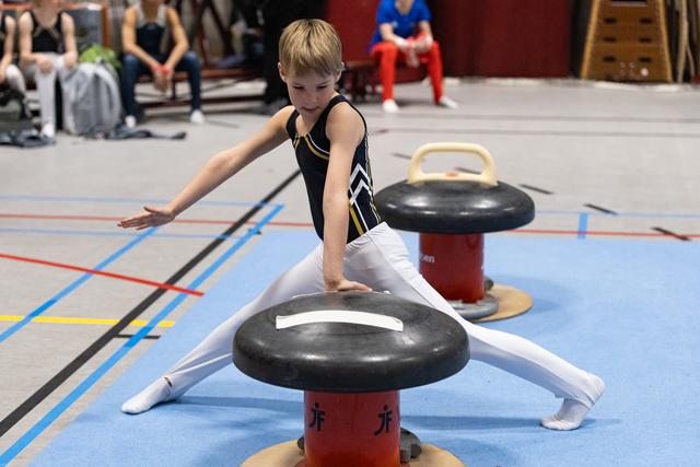 Young gymnast performs splits on red mushroom apparatus, concentrating on form with arms extended during training