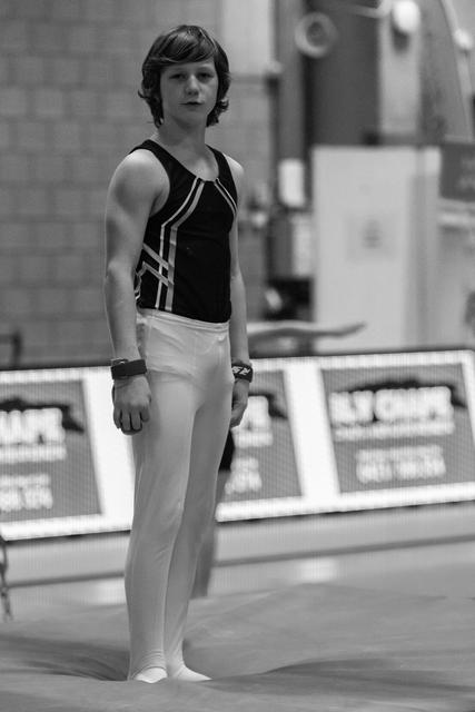Young male gymnast stands at attention in black and white uniform, focused and composed before his routine