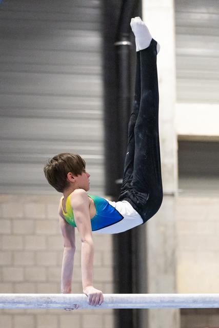 Young male gymnast performs a vertical handstand on the horizontal bar during training session