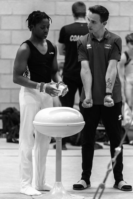 Coach in dark uniform consults with athlete in black and white beside chalk bowl during training session