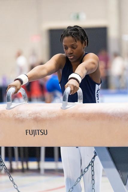 Female gymnast grips pommel horse handles with intense concentration during routine at Fujitsu-sponsored event