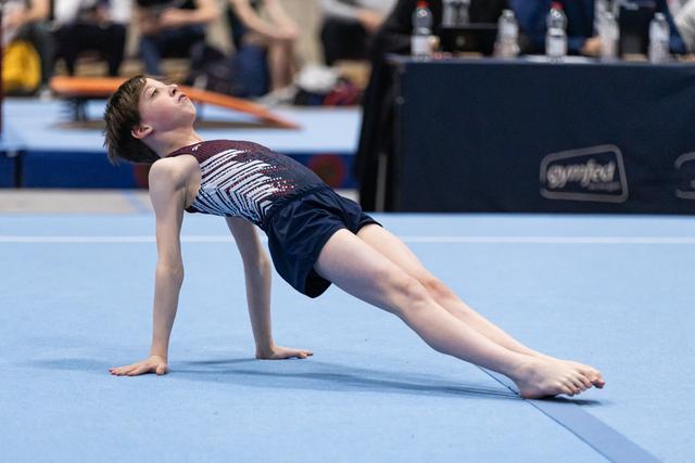 Young gymnast performs graceful backbend during floor routine, displaying strength and flexibility on blue mat