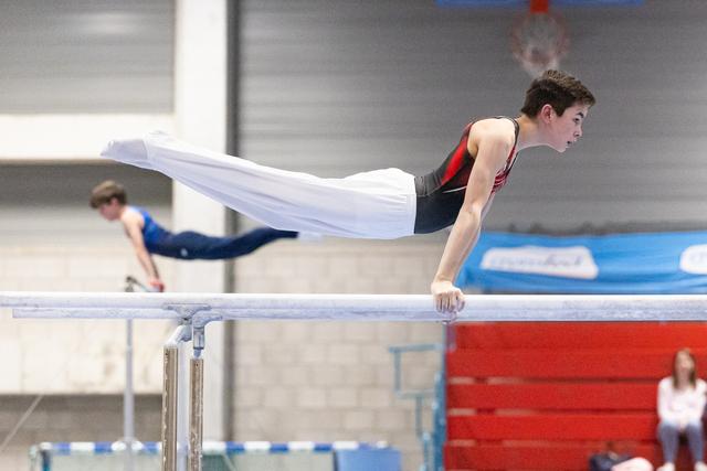 Young male gymnast holds a horizontal position on parallel bars during training, displaying strength and control
