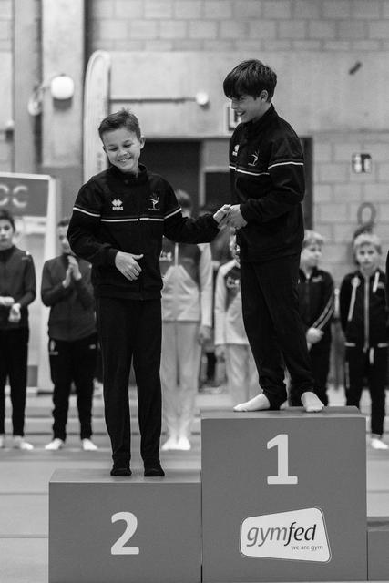 First and second place gymnasts shake hands on victory podium during medal ceremony at indoor gymnastics event