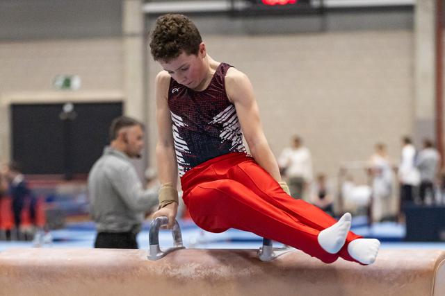 Male gymnast in sequined leotard performs pommel horse routine with focused expression in gymnasium