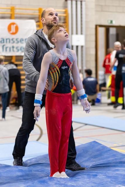 Young gymnast in red pants and coach both looking upward attentively during training in indoor gymnasium