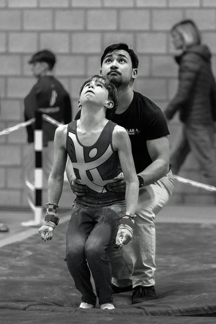 Young gymnast and coach looking upward together, coach supporting athlete from behind in focused anticipation