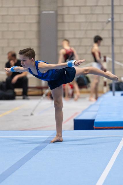 Young gymnast in blue leotard performs graceful arabesque balance on floor exercise mat during training session