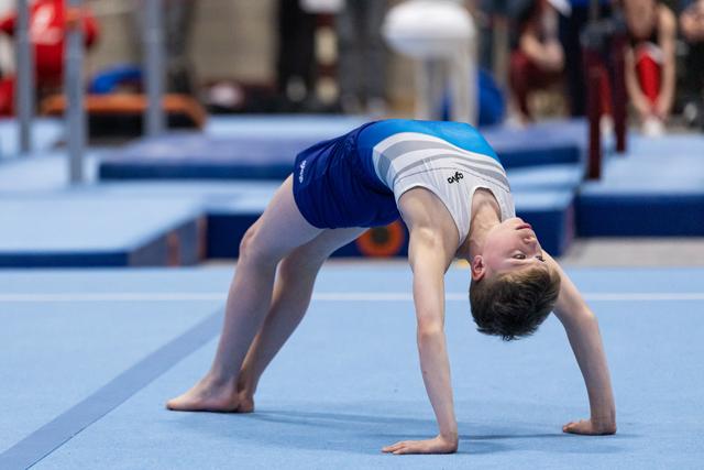 Young gymnast performs a backbend bridge position on blue gymnastics floor during training or warm-up