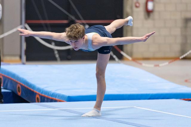 Young gymnast performs graceful balance pose with extended leg and arms on floor mat in training facility