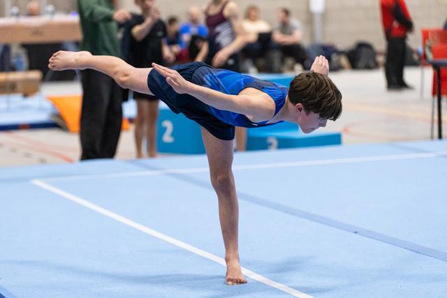 Young gymnast performs a precise arabesque balance on the blue floor mat, demonstrating focus and control during routine
