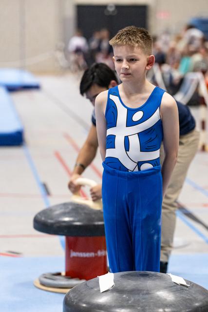 Young male gymnast in blue and white leotard stands beside vault apparatus, looking calm and focused before his routine