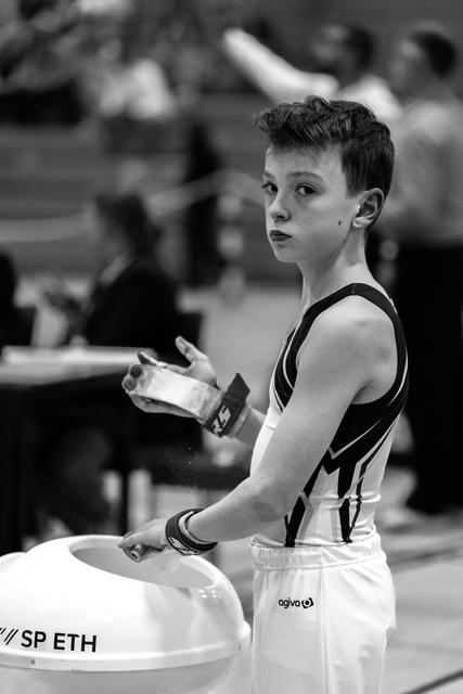 Young gymnast applies chalk to hands while standing beside vault apparatus, displaying focused concentration before performance