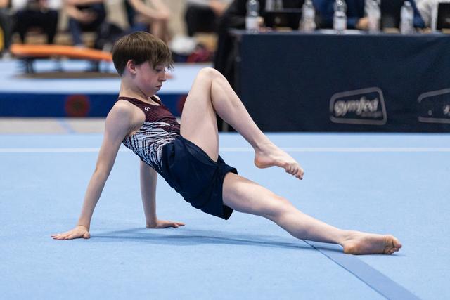 Young gymnast performs artistic floor element with extended leg position, displaying focus and flexibility during routine