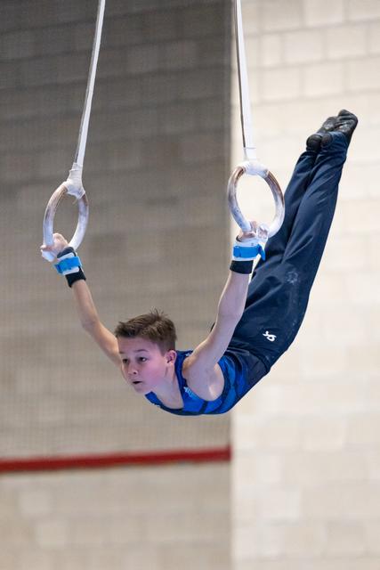 Young male gymnast performs an inverted pike position on rings, displaying strength and control in blue competition attire