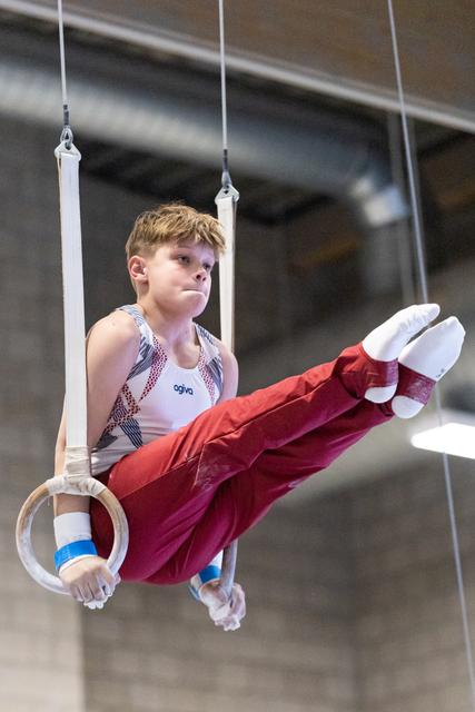 Young gymnast holds horizontal position on still rings with extended legs, showing concentration and strength