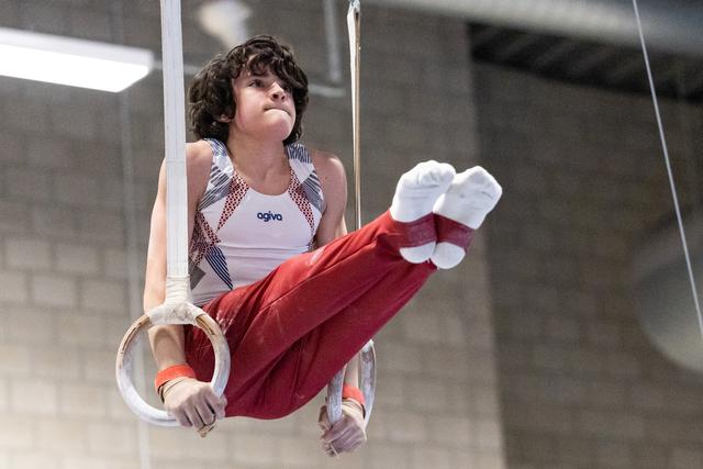 Young male gymnast performing rings routine with extended legs, displaying focus and strength during apparatus exercise
