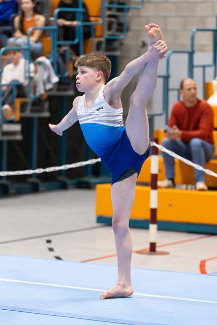 Young male gymnast performs an arabesque balance during floor exercise routine at indoor gymnastics meet