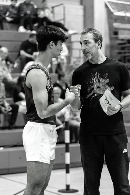 Coach and young boxer shake hands in mutual respect before a match, surrounded by spectators in the arena