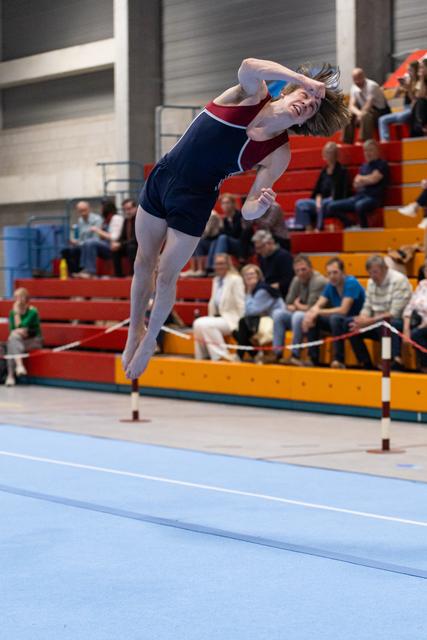 Gymnast performing dynamic backflip during floor exercise routine, arching backwards mid-air above blue mat