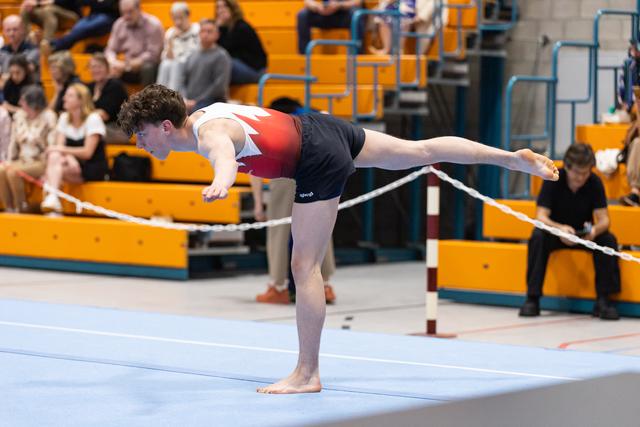 Young gymnast performs a horizontal scale balance on the beam, body fully extended parallel to the apparatus during routine