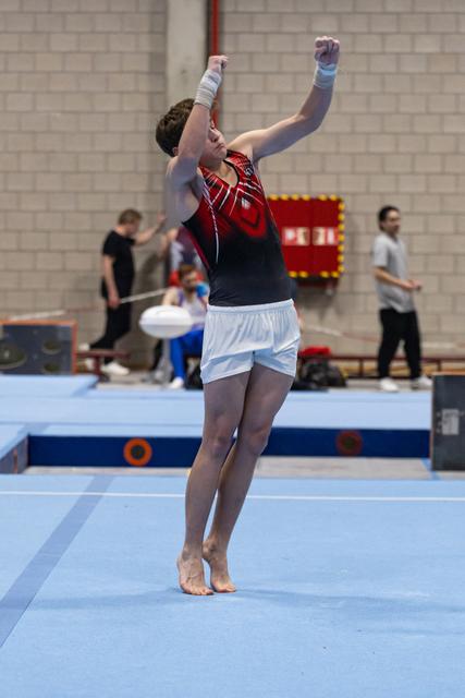 Gymnast celebrates with arms raised after completing floor routine, showing triumphant expression on training mat