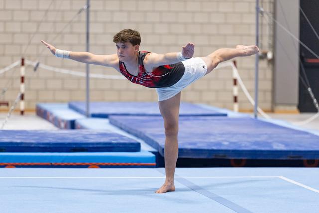 Young gymnast performs an arabesque balance on floor exercise, arms extended gracefully in a gymnastics training facility