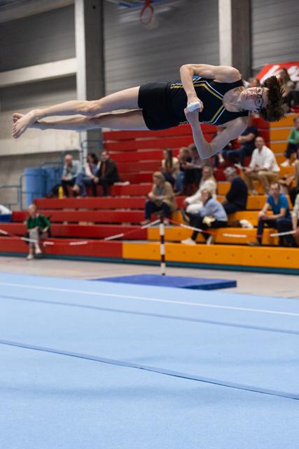 Gymnast performs horizontal backflip above blue floor mat with spectators watching from colorful bleachers