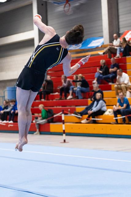 Gymnast executes dynamic tumbling pass with arched back mid-air on floor exercise in gymnasium competition